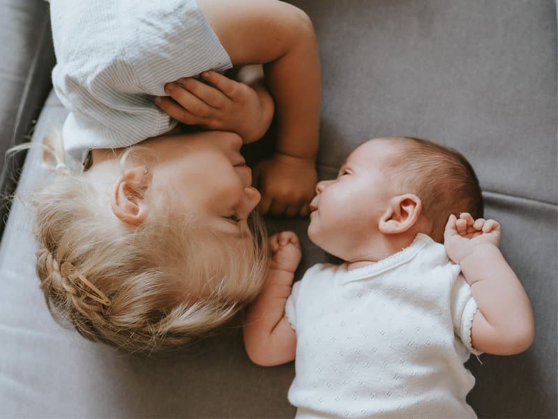 A toddler lying next to a newborn sibling, looking at each other