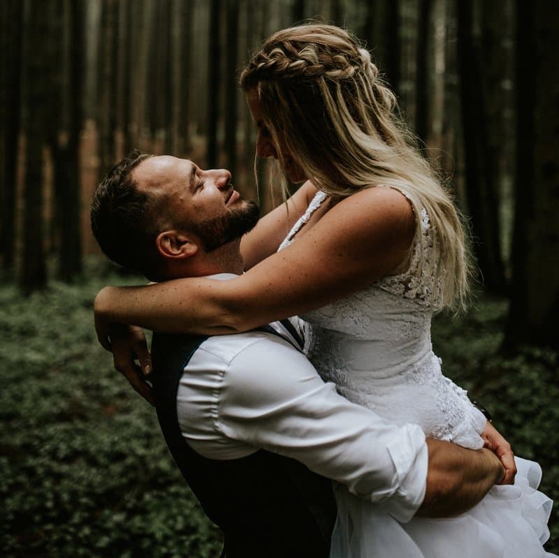 A groom holding his bride in a lace dress in the middle of a forest