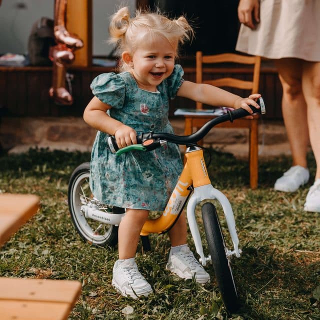 Little girl in a green dress on an orange balance bike in a garden at a birthday party